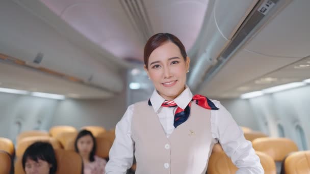 Retrato de la atractiva azafata asiática joven en uniforme mirando y sonriendo a la cámara en avión, tripulación de cabina o concepto de ocupación azafata - Imágenes, Vídeo