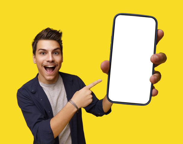 Smiling young and handsome man holding mobile phone with white screen, offering ample copy space. Image is isolated on clean white background, creating versatile canvas for various design needs. High - Foto, Bild