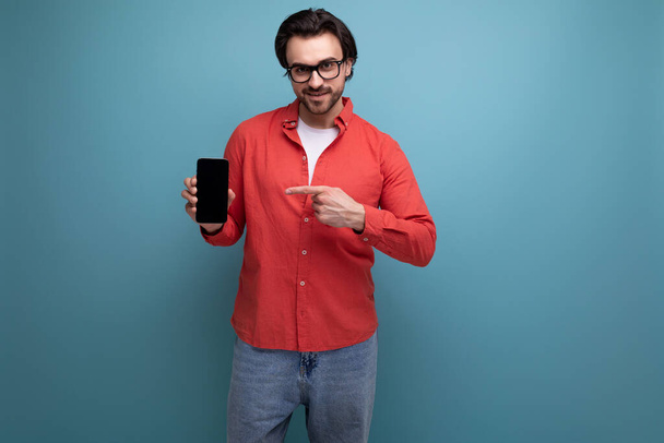 έξυπνος όμορφος νεαρός μελαχρινός άντρας με γυαλιά και κόκκινο πουκάμισο με smartphone. - Φωτογραφία, εικόνα