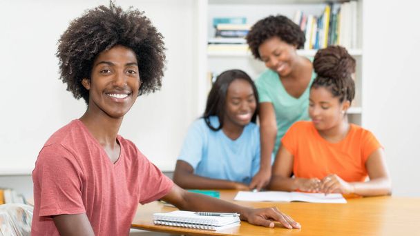 Laughing black male student at desk with group of learning african american students at classroom of college - Foto, Bild