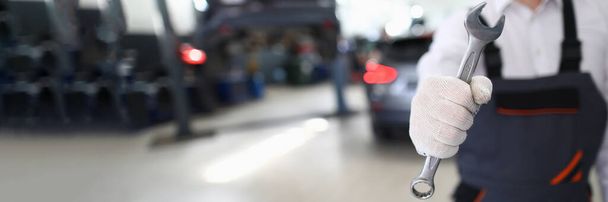 Επισκευαστής αυτοκινήτων με στολή κρατά κλειδί στο συνεργείο αυτοκινήτων. Αυτοκίνητο έννοια υπηρεσιών και αυτόματη υπηρεσία - Φωτογραφία, εικόνα