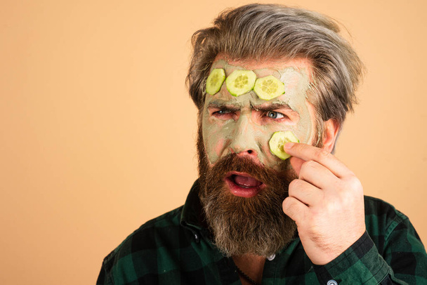 Man fun facial. Funny man with a clay mask. Male bearded model with face cream on the face. Man facial cucumber - Foto, afbeelding