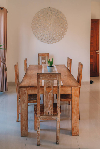 Holztisch mit Stühlen am Fenster mit Blick auf die Natur. Tropische Topfpflanze auf dem Tisch, balinesische Sommervilla - Foto, Bild