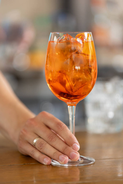 Piros koktél aperol egy szelet répával üvegben a csapos kezében egy bárpulton - Fotó, kép