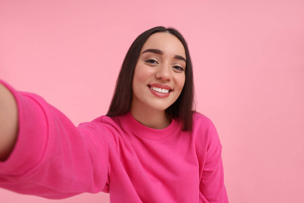 Smiling young woman taking selfie on pink background - Foto, afbeelding