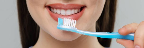 Woman brushing her teeth with plastic toothbrush on light grey background, closeup. Banner design - Fotografie, Obrázek