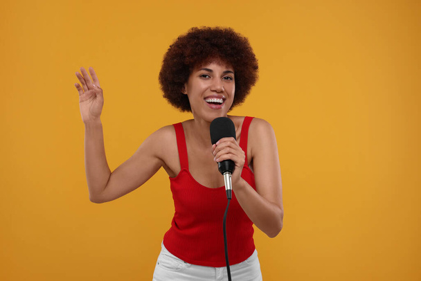 Mujer joven rizada con micrófono cantando sobre fondo amarillo - Foto, imagen
