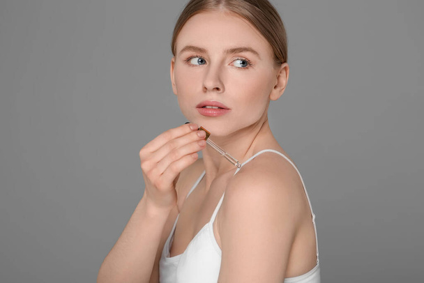 Beautiful young woman applying essential oil onto shoulder on grey background - Fotoğraf, Görsel