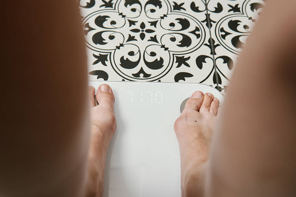 Holá žena kontroluje váhu váhy v koupelně. Žena měří svou váhu pomocí digitálních vah na podlaze. - Fotografie, Obrázek