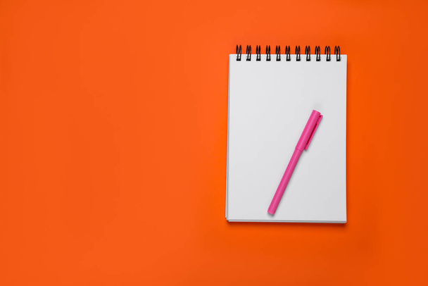 Leeres Büroheft und Stift auf orangefarbenem Hintergrund, Draufsicht. Raum für Text - Foto, Bild