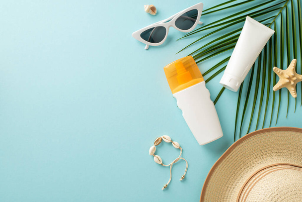 Embrace warmth of sun while protecting your skin. Top view of sunblock lotion and SPF cream tube without labels, eyeglasses, cap, shell bracelet, starfish, and a palm leaf on a pastel blue background - Photo, image
