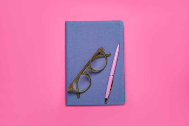 Blue office notebook, eyeglasses and pen on pink background, top view - Zdjęcie, obraz