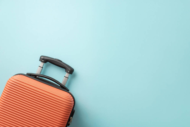 Verträumte Sommerreise. Orangefarbener Koffer von oben gesehen auf pastellblauem Hintergrund, der Platz für Text oder Werbung bietet - Foto, Bild
