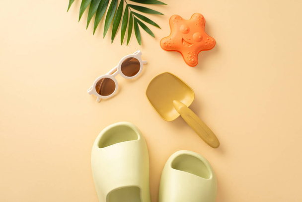 Tropical beach getaway with little one. Top view of beach toys, shovel, starfish sand mold, shades, slippers, palm leaf, soft beige backdrop. Perfect for promoting family-friendly vacation or product - Foto, afbeelding