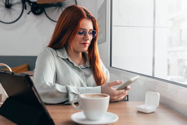 Redhead Girl. Red haired Beauty Engages in Remote Work at Trendy Caf - Photo, Image