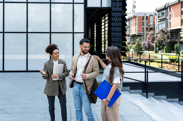 Quick briefing before meeting. Group of cheerful young successful business people talking to each other while walking outdoors. Office workers experts exchanging ideas and solutions - Foto, imagen