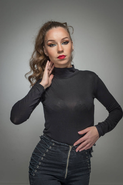 Attractive woman in black blouse and red lips  posing challenging in front of a background. Classic boudoir scene.  Sensual young  woman with long curly hair and black jeans wearing in front of camera - Foto, afbeelding