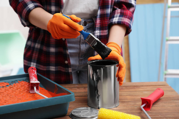 Woman dipping brush into can of black paint at wooden table indoors, closeup - Foto, Bild