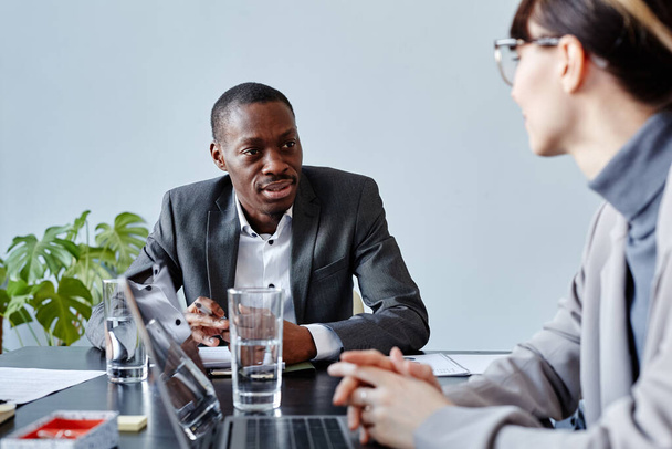 Portrait de jeune cadre afro-américain parlant à une collègue lors d'une réunion d'affaires au bureau contre un mur bleu pâle - Photo, image
