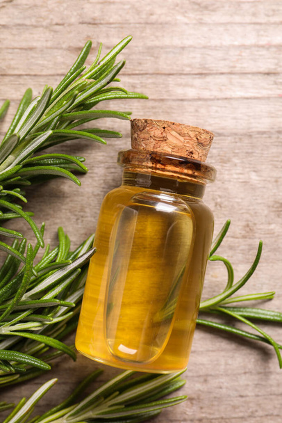 Bottle of essential oil and fresh rosemary on wooden table, flat lay - 写真・画像