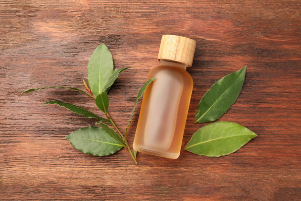 Bottle of bay essential oil and fresh leaves on wooden table, flat lay - Foto, imagen
