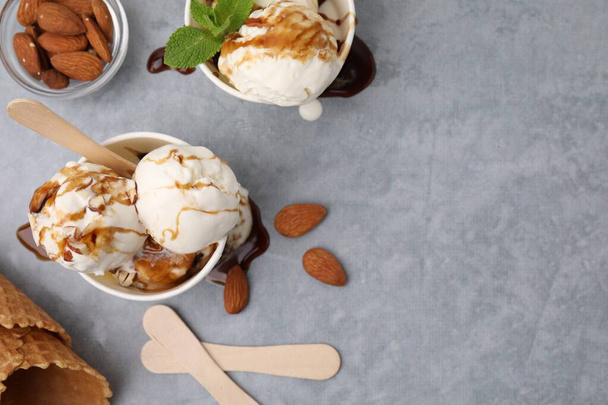 Scoops of ice cream with caramel sauce and nuts on light grey table, flat lay. Space for text - Fotografie, Obrázek