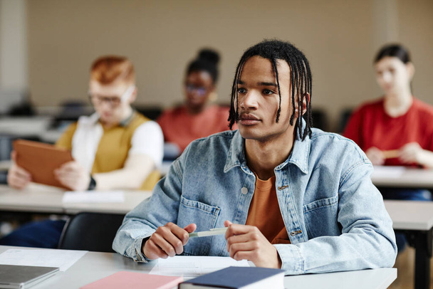 Portrét černého dospívajícího chlapce s copánky poslouchajícího přednášku ve škole nebo na vysoké škole, kopírovací prostor - Fotografie, Obrázek
