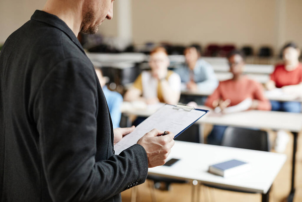 Close-up de professor universitário masculino verificando notas ao dar palestra para os alunos em sala de aula, espaço de cópia - Foto, Imagem