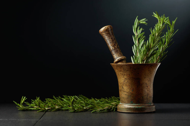 Old brass mortar with fresh rosemary branches. Black background with copy space. - Valokuva, kuva
