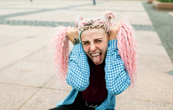 красива дівчина з рожевим жахливим волоссям показує язик на міській вулиці
. - Фото, зображення