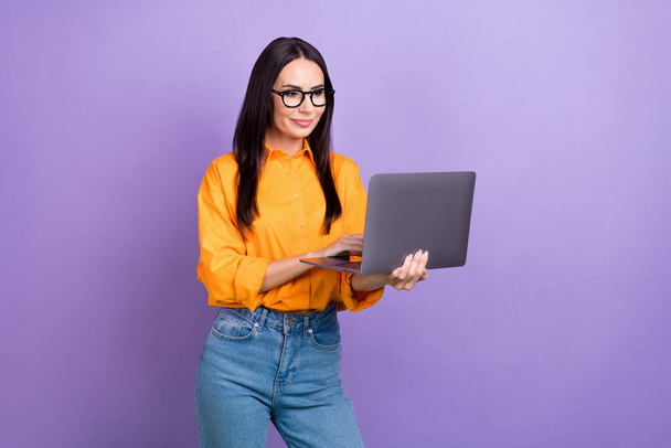 Photo of young confident entrepreneur woman wear orange shirt hold laptop zoom meeting work moment isolated on violet color background. - Фото, изображение