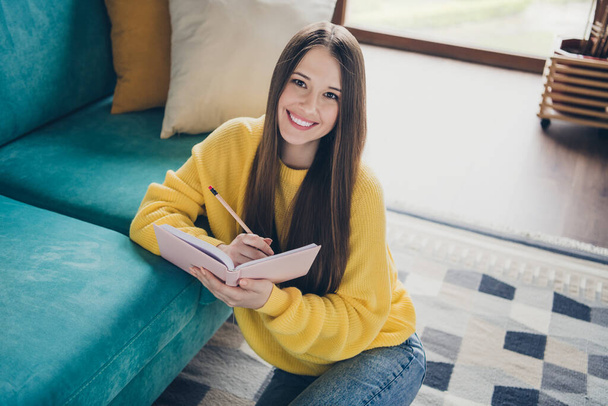 Portrait of lovely satisfied young girl toothy smile sitting carpet floor hold pencil notepad bright apartment inside. - Fotó, kép