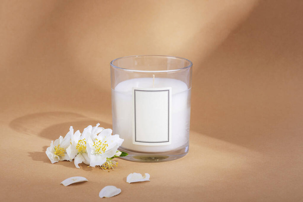 White aroma candle and jasmine flowers on beige background with light and shadows. Closeup. - Фото, зображення