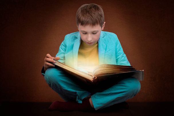 Il ragazzo sta leggendo un libro con un bagliore magico. - Foto, immagini