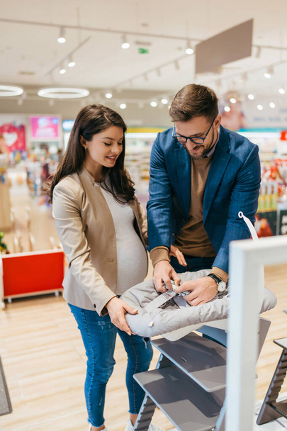 Attractive middle age couple enjoying in buying baby cradle swing. Heterosexual couple in a baby shop or store. Child expecting concept. - Foto, Bild