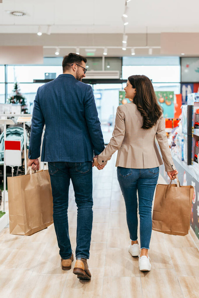 Satisfied and happy couple leaves a baby store with shopping bags. Parenthood and child expecting concept.  Back view. - Foto, Imagem