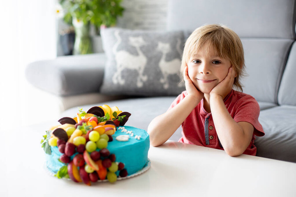 Cute preschool boy with birthday cake with candles at home, preparing for party with friends and siblings - Foto, afbeelding