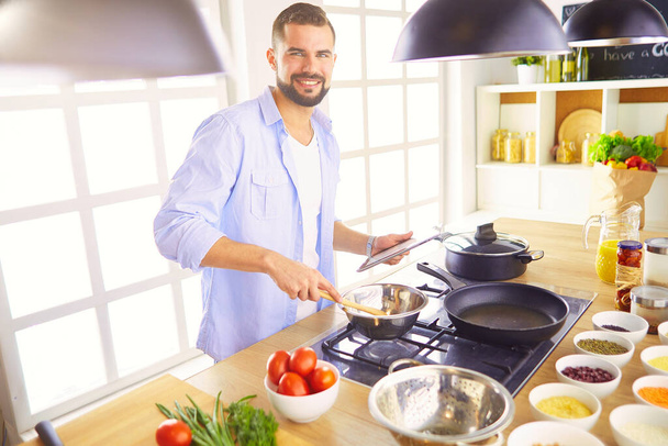 Muž po recept na digitální tablet a vaření chutné a zdravé jídlo v kuchyni doma. - Fotografie, Obrázek