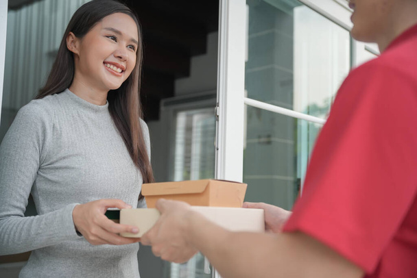 Happy smiling woman receives boxes parcel from courier in front house. Delivery man send deliver express. online shopping, paper containers, takeaway, postman, delivery service, packages - Fotó, kép