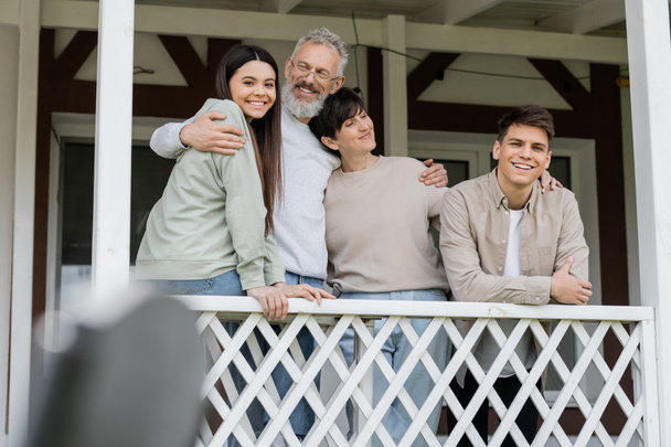 parents day, middle aged parents hugging daughter and young adult son on porch of summer house, family celebration, bonding, modern parenting, moments to remember, reunion  - Photo, Image