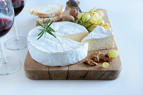 Brie cheese with nuts, grapes and wine on a wooden cutter board on white background. Camembert cheese.  - Photo, Image