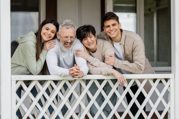 parents day, middle aged parents hugging with teenage daughter and young adult son on porch of family house, celebration, bonding, modern parenting, moments to remember, laughter  - Photo, Image