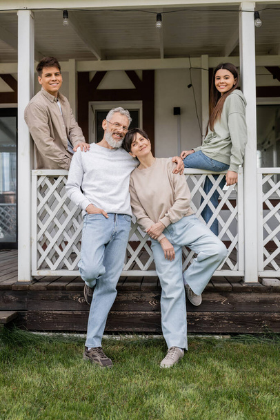 family photo, parents day, middle aged parents posing next to daughter and young adult son on porch of summer house, family celebration, bonding, moments to remember, modern parenting  - Photo, Image
