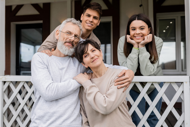 family photo, happy parents day, middle aged parents hugging near teenage daughter and young adult son on porch of summer house, family celebration, bonding, moments to remember, modern parenting  - Photo, Image