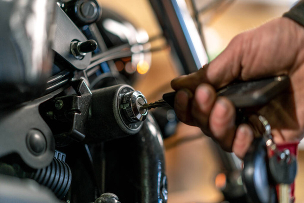 Autentica officina motociclistica creativa Motociclista meccanico in garage mettendo la chiave nella scatola di alimentazione per avviare la moto da vicino - Foto, immagini