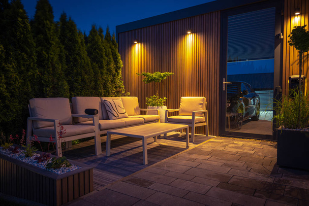 Lounge e área de jantar no moderno quintal residencial decorado com luzes ao ar livre, plantas, mesa de jardim e cadeiras. Noite de Verão aconchegante. - Foto, Imagem