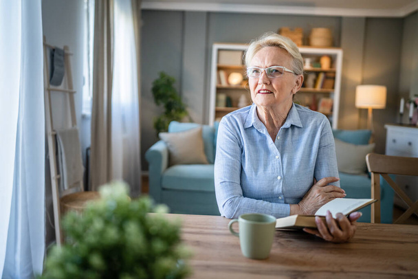 One woman mature senior caucasian female pensioner modern grandmother read book at home wear eyeglasses real person copy space - Fotó, kép