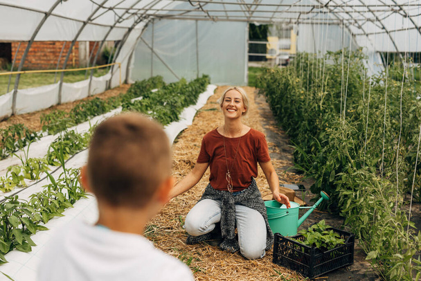 Happy mother works in a greenhouse and smiles when she sees her son coming. - Fotografie, Obrázek