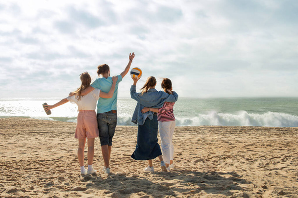 Satisfecho millennial árabe y europeos en casual con pelota divertirse, abrazos, disfrutar de la libertad, música en la playa en fin de semana al aire libre. Vacaciones y caminar juntos con amigos, anuncio y oferta - Foto, Imagen