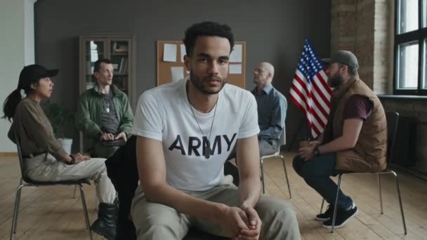 Selektivní zoom v portrétu mladého černocha sedícího proti podpůrné skupině PTSD hledícího do kamery - Záběry, video